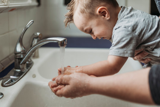 Side view of young toddler having hands washed in sink by dad