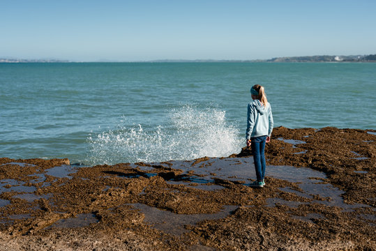 Tween girl watching waves splash over rocks in New Zealand