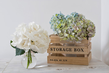 A large branch with green and blue pastel hydrangea in a storage wooden box on a beige table.