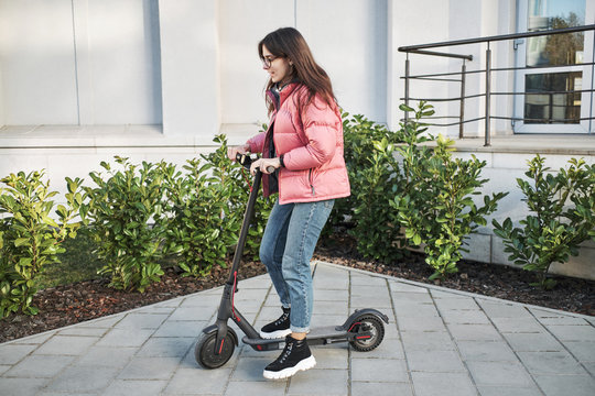 millennial young girl in a pink jacket on an electric scooter