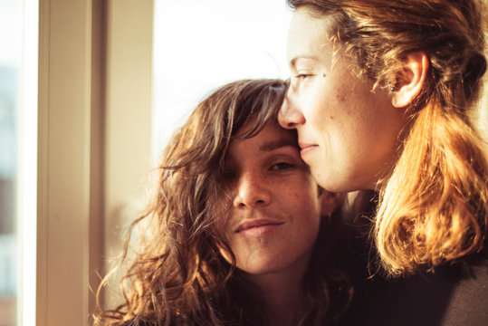 feminine lesbian couple watch the sun set through window in warm loft