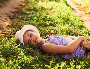 Beautiful long hair fun kid girl lying on the grass and enjoying green grass summer sunny background. Closeup
