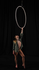 Fototapeta na wymiar Beautiful graceful girl, aerialist. professional circus acrobat on an aerial hoop. performer holding a ring in his hands, black background. black curtain backstage with pleats, rehearsal, grace.