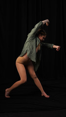 Young athletic girl dancer posing on a black background. the artist performs a contemporary dance. slim model choreography in studio on black background