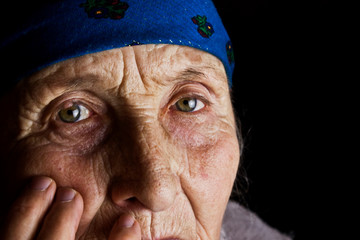 Eyes of an old grandmother close-up. Wrinkled face of an old mother in the dark closeup portrait photo. Caring for old people. Do not leave parents. Gray hair and wrinkles of an old grandmother