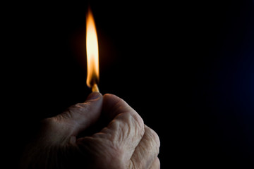 Burning match in the dark close-up. Burning match in the old wrinkled hand of the grandmother in the dark. Time is fleeting. Fire in the dark in old hands close-up