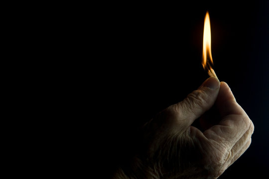 Flaming fire in the dark close-up. Old grandmother holds a match burning in the dark close-up. Conceptual photo time is fleeting. Burning match in old hands in the dark.