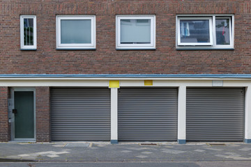 Front view of entrance of the building and shutter doors of garages under typical design of housing or apartment in Europe with rectangular windows and vintage brick facade.   