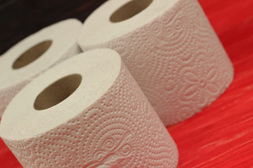 Three rolls of white toilet paper on red background with space for text. Deficit means of hygiene during coronavirus