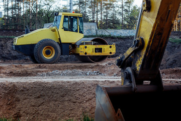 Heavy Vibration roller without a driver on a sand road as an example of rest between road works. The bucket of the excavator in the foreground.