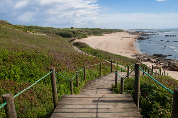 A wooden staircase leading to the white sand beach. Landscape, panorama of the ocean, beach and coastline, green grass. 
