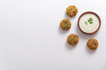 Homemade falafel served in a plate with Tzatziki sauce in a wooden bouwl. With Cilantro and parsley. White background.
