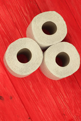 Three rolls of white toilet paper on red background with space for text. Deficit means of hygiene...