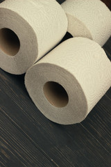 Three rolls of white toilet paper on wooden background with space for text. Deficit means of hygiene during coronavirus
