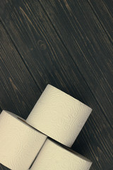 Three rolls of white toilet paper on wooden background with space for text. Deficit means of hygiene during coronavirus