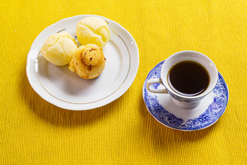 Brazilian cheese bread and coffee cup and on the yellow mat.