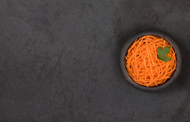 Vegetable appetizer carrots cut into thin straws in a wooden bowl on a dark background top view...