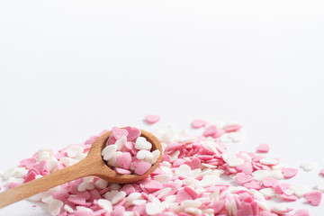 Spoon full of sweet decorative pink and white hearts. Baking decorations, Sugar hearts in a wooden measuring spoon, close up.