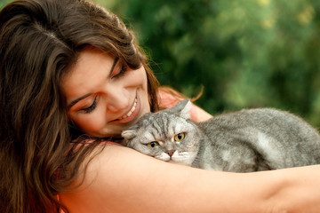 Cheerful beautiful brunette girl in the park is sitting with a cat. happy photoshoot with a pet cat on the street..