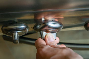 woman's hand turns on a switch on a stainless steel gas stove close up, view top