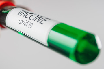 Vacuum tube with a sample of Covid-19 vaccine of green color in the hand with a medical glove on a white background