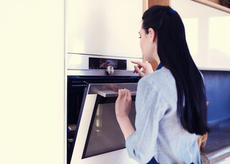 Beautiful young woman checking how her cake is doing in the oven