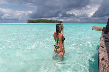 Young woman in shallow water looking at tropical island.