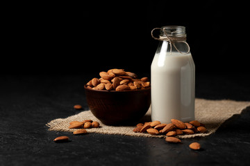 one bottle of almond milk on a dark black background with nuts, vegetarian milk without sugar and lactose