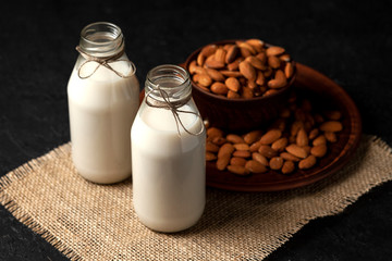 almond milk without sugar and lactose in bottles with sprinkled nuts, vegetarian milk drink on a black table