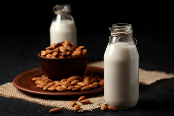 almond milk without sugar and lactose in bottles with sprinkled nuts, vegetarian milk drink on a black table