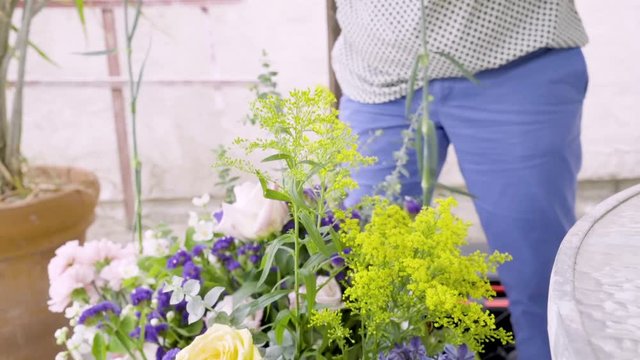 Florist working in her backyard picking pink, white, and purple flowers with green stems for a bouquet.