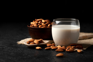 glass of almond milk without lactose and sugar with sprinkled nuts, a veggie milk drink on a black table