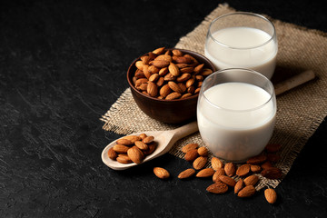 almond milk in a glass with nuts on a dark background, a healthy dairy product without lactose on a black table