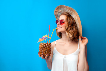 girl in summer clothes drinks a tropical pineapple cocktail and smiles on a blue isolated...