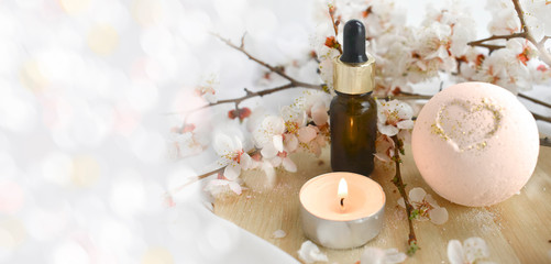Aromatherapy concept with essential oil bottle, bath bomb, burning candle and blossoms branch. Spa or herbal medicine still life composition. Copyspace.