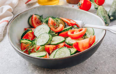 Healthy vegetable salad of fresh tomato, cucumber, dill and spices and oil in bowl on light gray background. Diet concept.