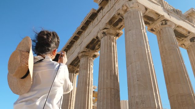 Young Woman taking pictures at Parthenon, Acropolis of Athens, Greece. Large hat, fashion white dress, sunglasses, vintage camera.