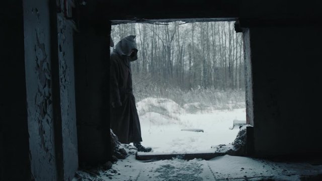 strange man walk walking in the apocalyptic destroyed space military base in dark raincoat with hood  stalker winter isolation isolated after covid19