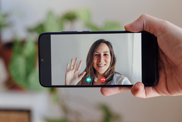 Friend saying Hi in a zoom videocall, hand holding phone while making a video call