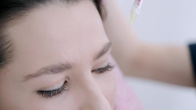 Woman has dark hair. Cosmetologist makes botox injection. Girl is in beauty salon.