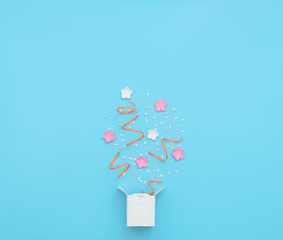 White box with party confetti, streamers and flowers explosion on blue background. Mother day, Valentine day, Wedding, Birthday party concept. Greeting or invitation card. Flat lay with copy space.