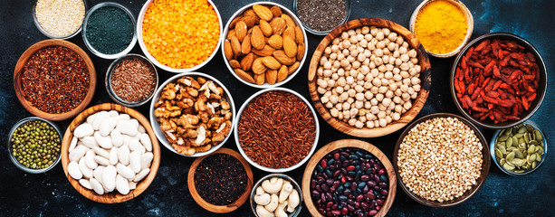 Superfoods, legumes, nuts, seeds and cereals selection in bowls on grey background. Superfood as chia, spirulina, beans, goji berries, quinoa, turmeric, mung bean, buckwheat, lentils, flax seed