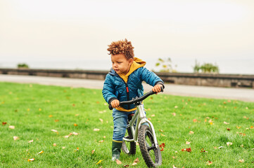 Funny toddler boy riding a bike in park, cute african kid having fun outside on a nice autumn day