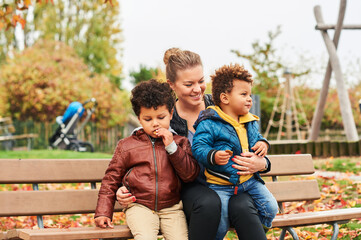 Outdoor portrait of happy young mother with two lovely sons, family enjoying nice autumn day in...