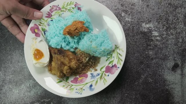 "Nasi Kerabu" been put on the table. "Nasi kerabu" is blue-coloured rice is eaten with dried fish or fried chicken, crackers, pickles and other salads.