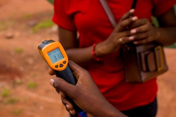 young black woman's hand holding a handheld infrared thermometer