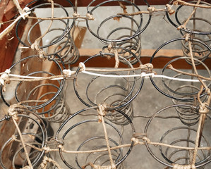 Fototapeta na wymiar Rusted metal wire chair coils exposed in an antique wooden chair seat. Rows of metal spirals with jute twine rope. Laid out in an array of pattern. Chair is a vintage rocker.