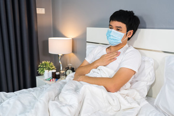 sick man in medical mask suffering from virus disease and fever in bed, coronavirus (covid-19) pandemic concept.