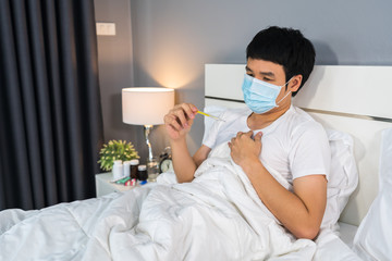 sick man in medical mask using thermometer to checking his temperature on bed, coronavirus...