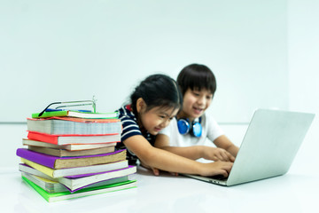 Large stack of the books and blurred children playing laptops. Distance education. Network and connection. Children and learning concept. Concept of Studying at home and Technology.